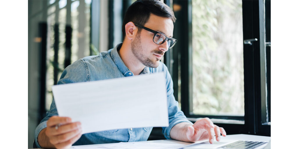 Thoughtful young businessman reviewing payroll numbers on his laptop